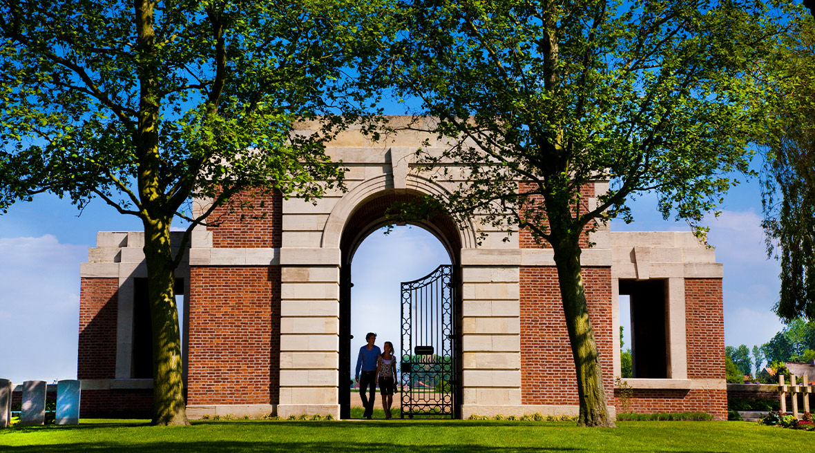 The entrance arch to Lijssenthoek Military Cemetery, flanked by trees.